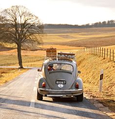 an old car is driving down the road in front of a field with trees and grass