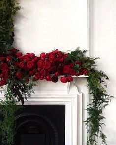 a fireplace with red flowers and greenery on the mantle