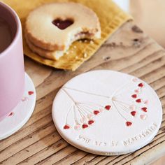 a cup of coffee next to a cookie on top of a wooden table with writing