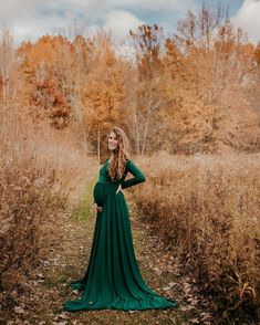 a pregnant woman in a long green dress poses for the camera with her hands on her hips