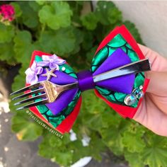 a hand holding a purple and green bow tie with two forks attached to the top