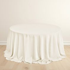 a round table with a white cloth draped over it on top of a hard wood floor