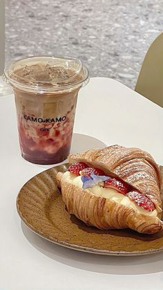 a croissant sandwich on a plate next to a cup of yogurt