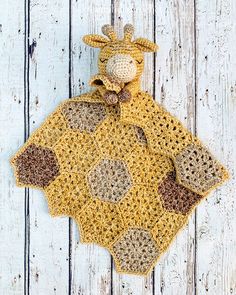 a crocheted giraffe is sitting on a white wooden surface with a yellow and brown blanket