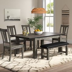 a dining room table with chairs and a bench in front of a window on a rug