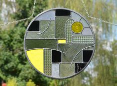 a circular stained glass sun catcher hanging from a chain with trees in the back ground