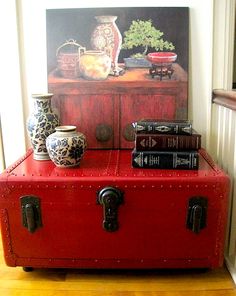 a red suitcase sitting on top of a hard wood floor next to a painting and vases