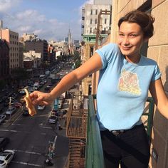 a woman standing on top of a balcony next to a street filled with traffic and tall buildings