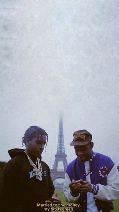 two men standing in front of the eiffel tower looking at their cell phones