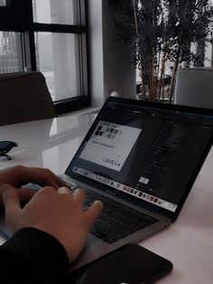 a person using a laptop computer on a white table in front of a large window