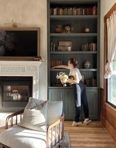 a woman standing in front of a bookshelf holding a vase with flowers on it