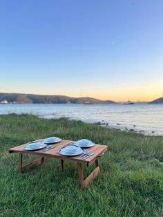 two plates sit on a wooden table in the grass by the water with mountains in the background