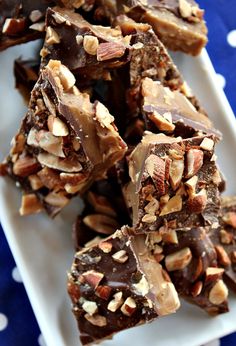 a white plate topped with pieces of chocolate covered in nuts and pecans on top of a blue table cloth