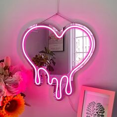 a pink heart shaped neon sign hanging from the side of a wall next to a vase with flowers