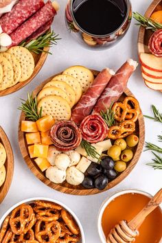 an assortment of snacks and crackers in wooden bowls on a white table with wine