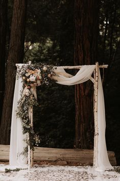 a wedding arch decorated with flowers and greenery for an outdoor ceremony in the woods