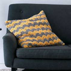 a black couch with a yellow and gray crochet pillow on top of it