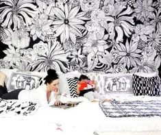 a woman laying on top of a bed next to a black and white wallpaper