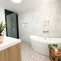 a white bath tub sitting next to a wooden stool in a bathroom under a ceiling light