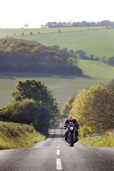 a person riding a motorcycle down the middle of an empty road with fields in the background