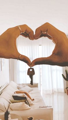 two hands making a heart shape over a couch with a key in the other hand