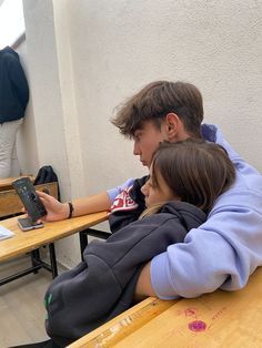 two people sitting at desks using their cell phones and looking at papers on the table