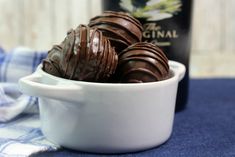 three chocolate truffles in a white bowl next to a bottle of wine