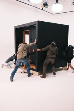 three people are trying to climb into a small black box in the middle of a room