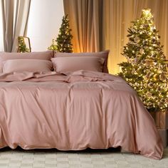 a bed with pink sheets and pillows next to a christmas tree