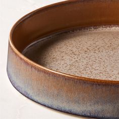 a close up of a brown and blue bowl on a white table top with water in it