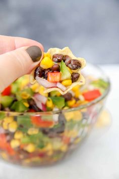 a hand holding a tortilla filled with black beans, corn and avocado