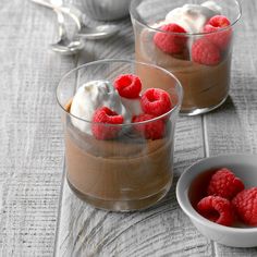 two desserts with raspberries and whipped cream in small glass bowls on a table