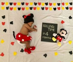 a baby laying on top of a bed next to mickey mouse stuffed animals and a sign reading rolling time 4 months