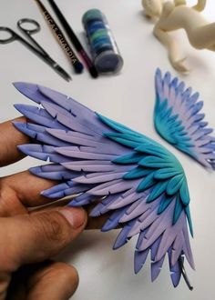 a person is holding some fake feathers on a table next to scissors and other crafting supplies