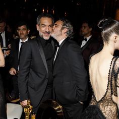 two men in tuxedos are kissing each other at an oscars event with others looking on