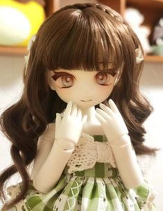 a doll with long brown hair wearing a green dress and holding her hands to her face