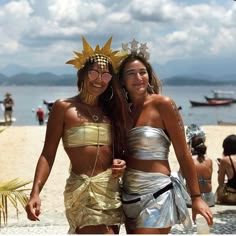 two women in costumes standing on the beach with their arms around each other and smiling at the camera