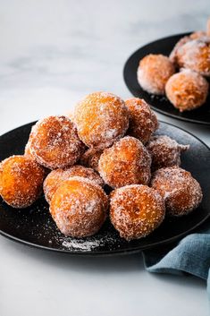 powdered sugar covered donuts on black plates next to another plate with blue napkin