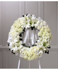 a wreath with white flowers and greenery hanging on a stand in front of a door