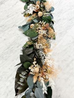 an arrangement of flowers and greenery is arranged on a white marble countertop for display