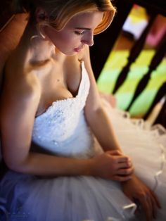 a woman in a white dress is sitting on a chair and looking down at something