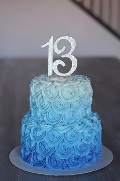 a blue and white tiered cake with the number thirteen on it's top