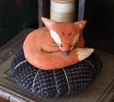 an orange fox sleeping on top of a blue and black cushion next to a spool of thread