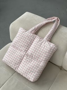 a pink and white checkered bag sitting on top of a couch next to a pillow