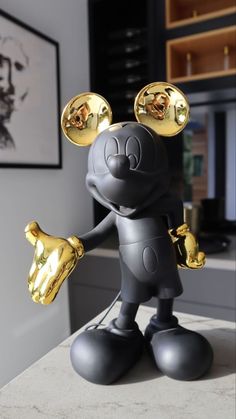 a mickey mouse figurine holding two gold bell shaped objects in his hand and standing on top of a counter