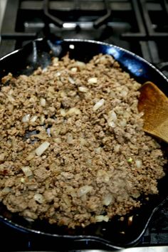 a skillet filled with meat and onions on top of a stove next to a wooden spoon