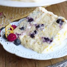 a slice of cake on a plate with raspberries and blueberries next to it