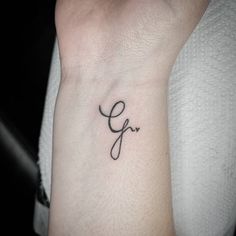 a small wrist tattoo with the letter g in cursive font on it's left arm