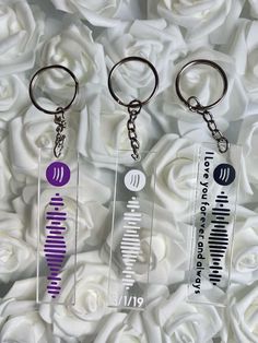 three key chains with different designs on them sitting in front of white rose bushes