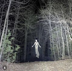 a woman is walking through the woods at night